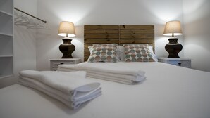 A neatly made bed with white linens, two bedside tables with lamps, a wooden headboard, and a hanging clothes rack. - T3 Carcavelos by the sea - Cascais / Lisbon / Sintra (Carcavelos)
