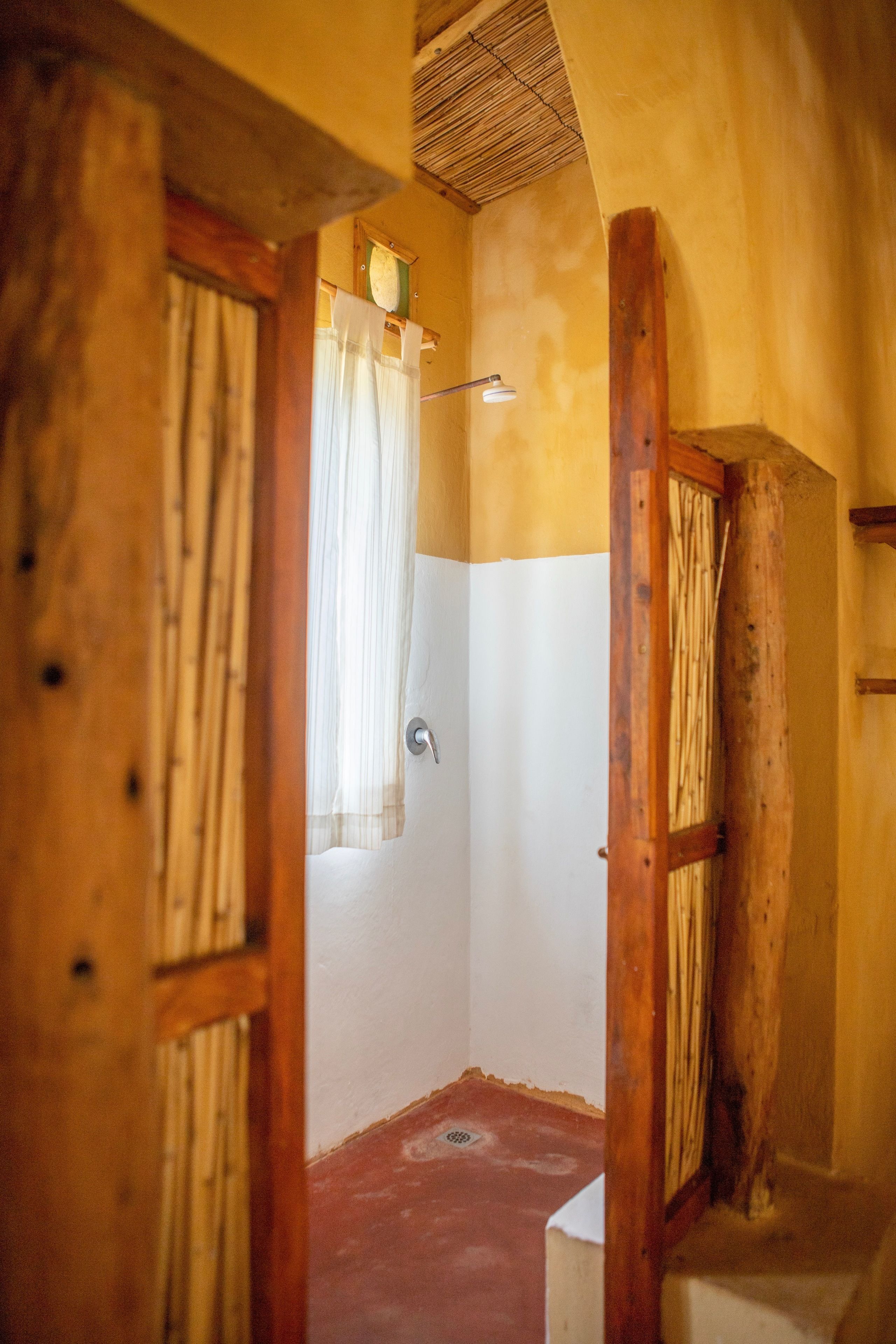 Une salle de bain rustique avec des poutres en bois, une douche et une fenêtre avec des rideaux.