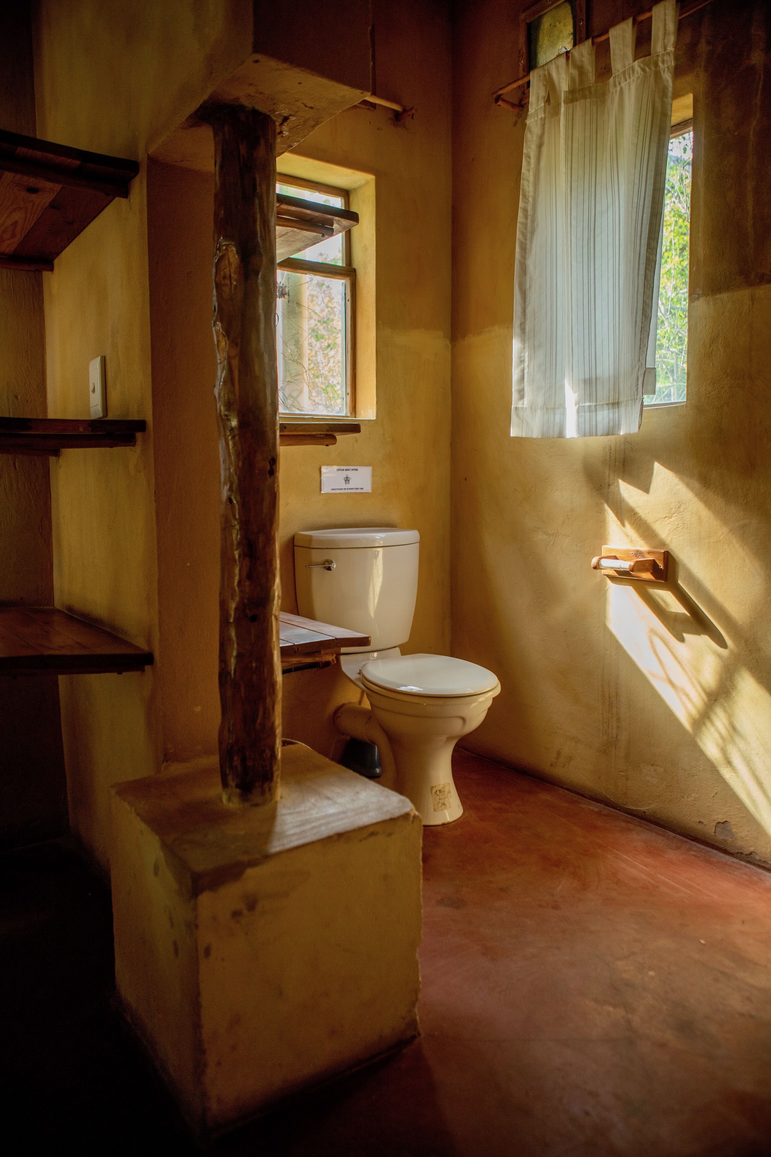 Ein rustikales Badezimmer mit Holzbalken, Toilette und einem Fenster mit Vorhang.