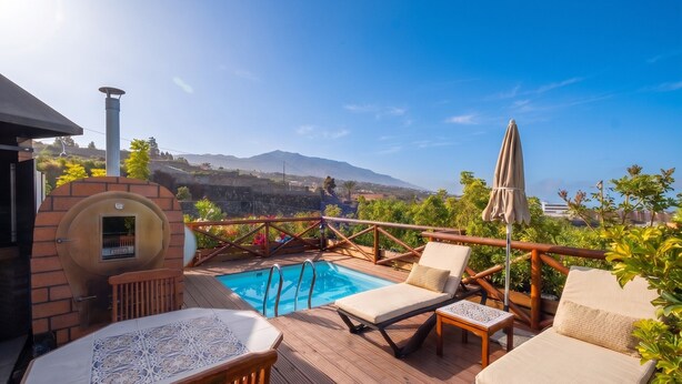 A poolside area with a barbecue, lounge chairs, and a view of mountains.