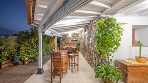 An outdoor dining area with a stone wall, wooden furniture, and potted plants.