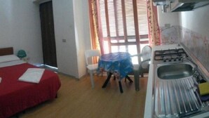 A bedroom with a bed, a small table with a chair, and a kitchenette area with a sink and stove. - APARTMENT / STUDIO PALINURO CENTER AT 800M FROM THE SEA ....................... (Palinuro)