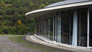 Un edificio moderno con fachada de vidrio curvada, techo de hormigón y un camino de grava que conduce a él.