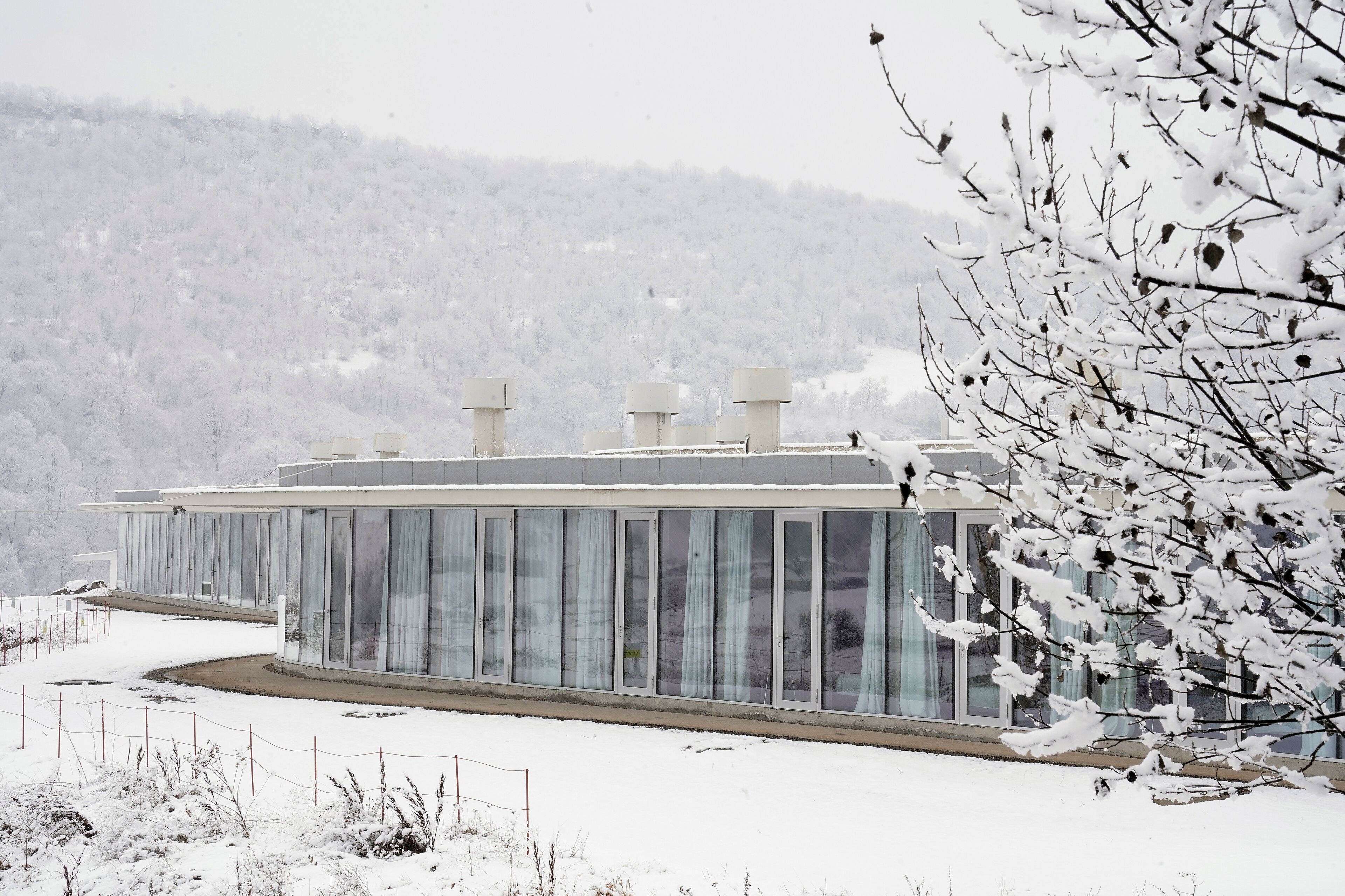 Un edificio moderno con grandes ventanales, techo plano y un paisaje nevado al fondo.