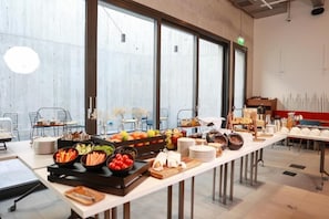 A buffet setup with various food items and a long table in a modern interior with large windows.