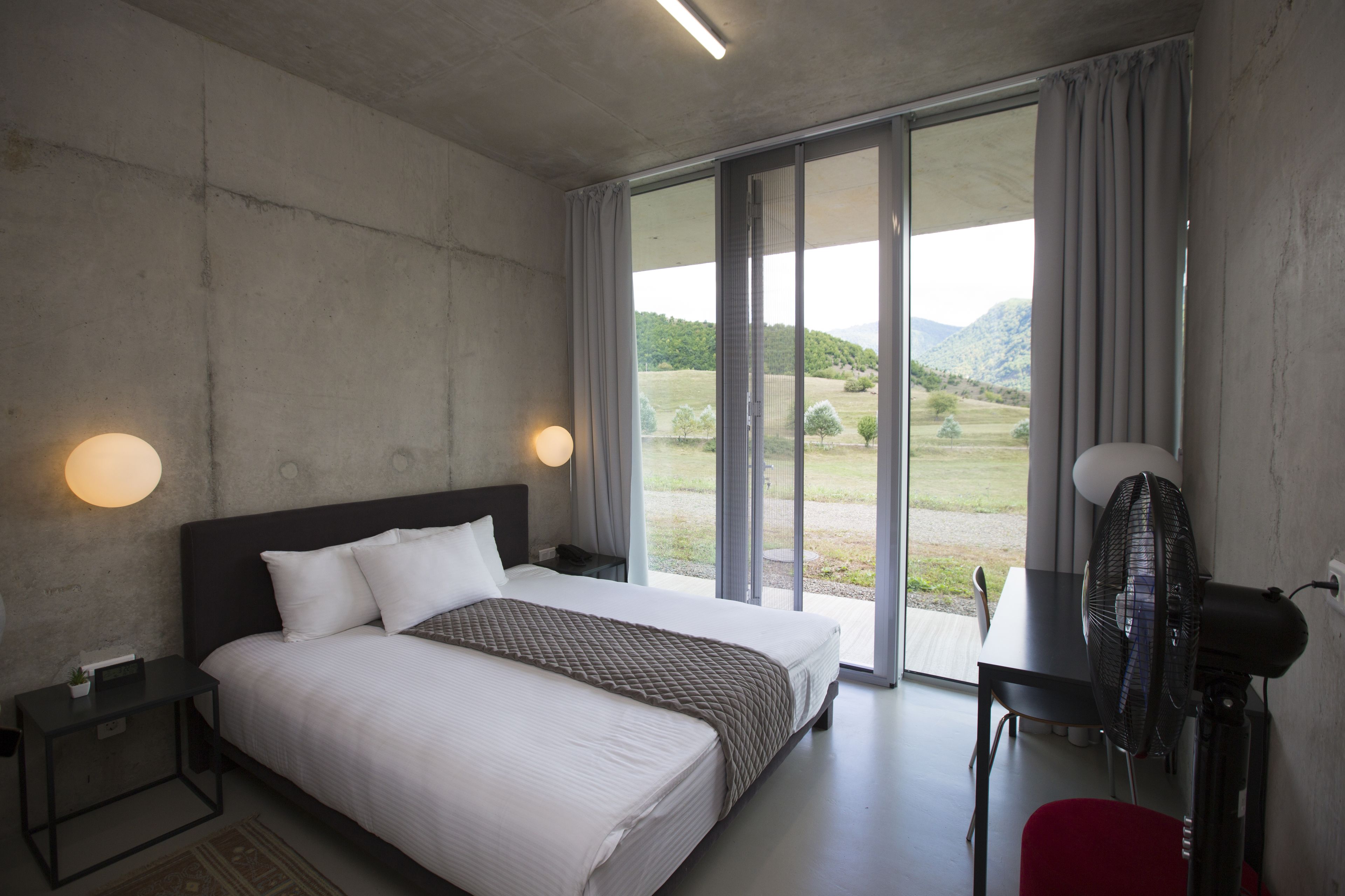 Une chambre moderne avec un grand lit, un bureau et une vue sur un paysage verdoyant par la fenêtre.