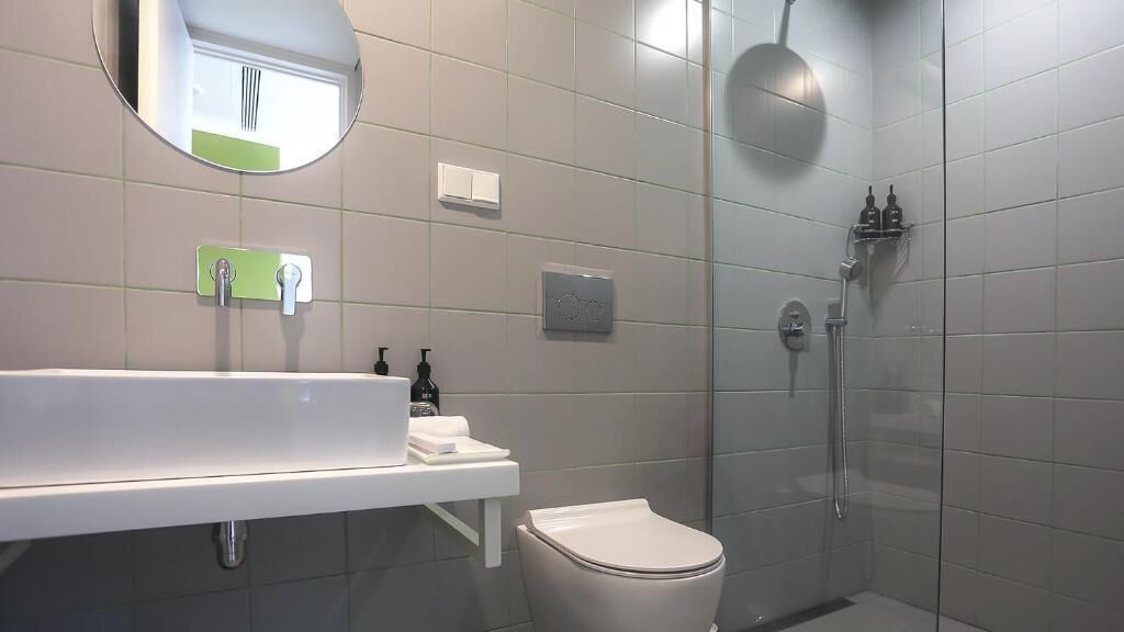 Un baño moderno con un lavamanos blanco, un inodoro, un box de ducha y un espejo.
