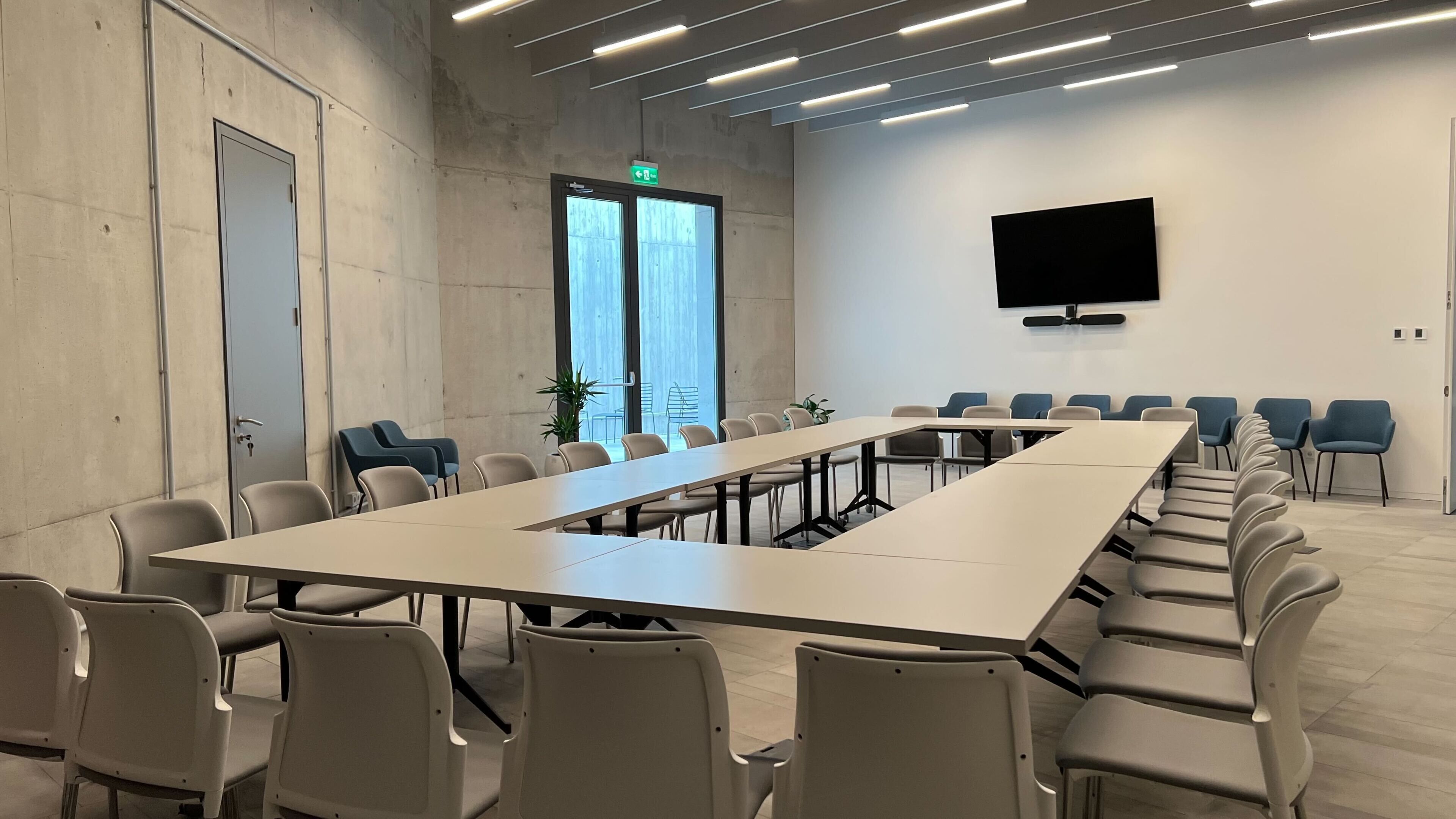 Una sala de conferencias con una larga mesa, sillas, un televisor de pantalla plana y una puerta con letrero de salida.