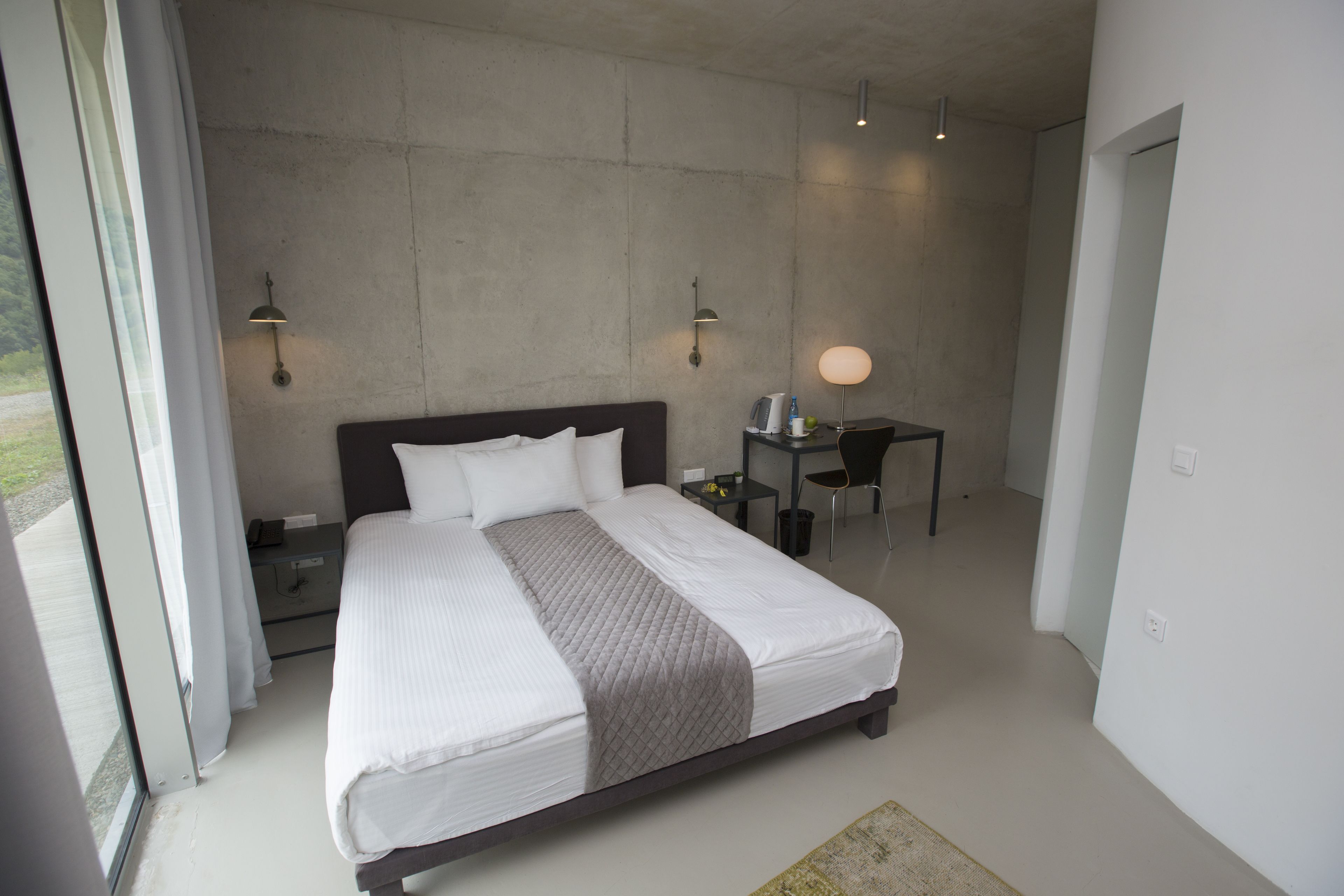 A modern bedroom with a large bed, bedside tables, a desk, and a chair.