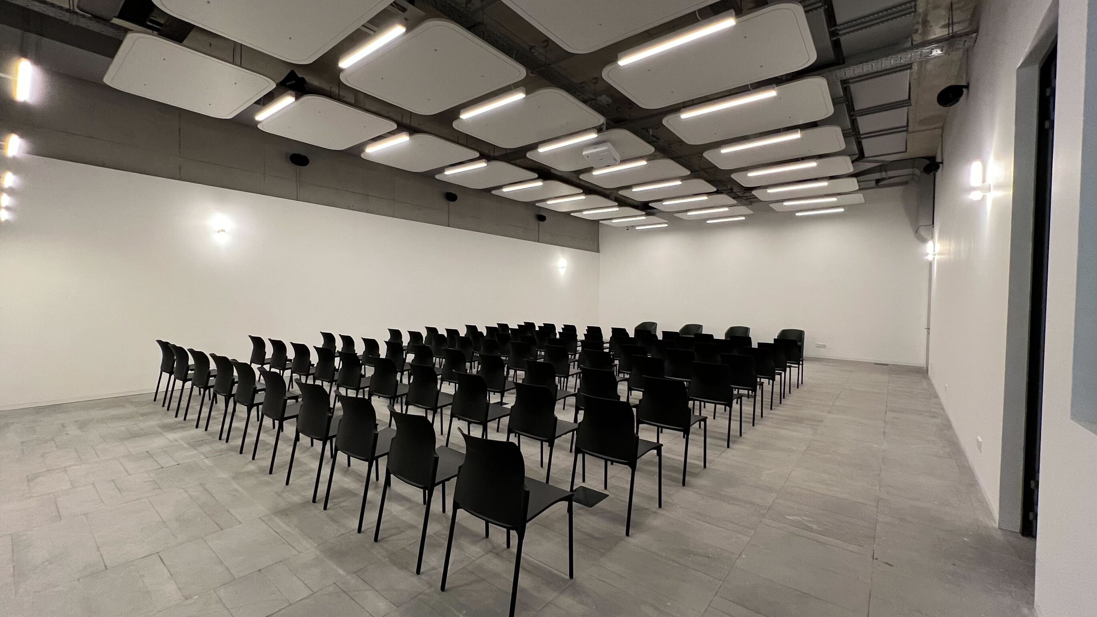 Konferenssihuone, jossa on riveissä mustia tuoleja ja valkoinen katto, johon on upotettu valaisimia.