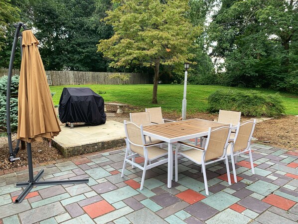 Une terrasse extérieure avec une table et des chaises, un barbecue abrité et une clôture en bois en arrière-plan.