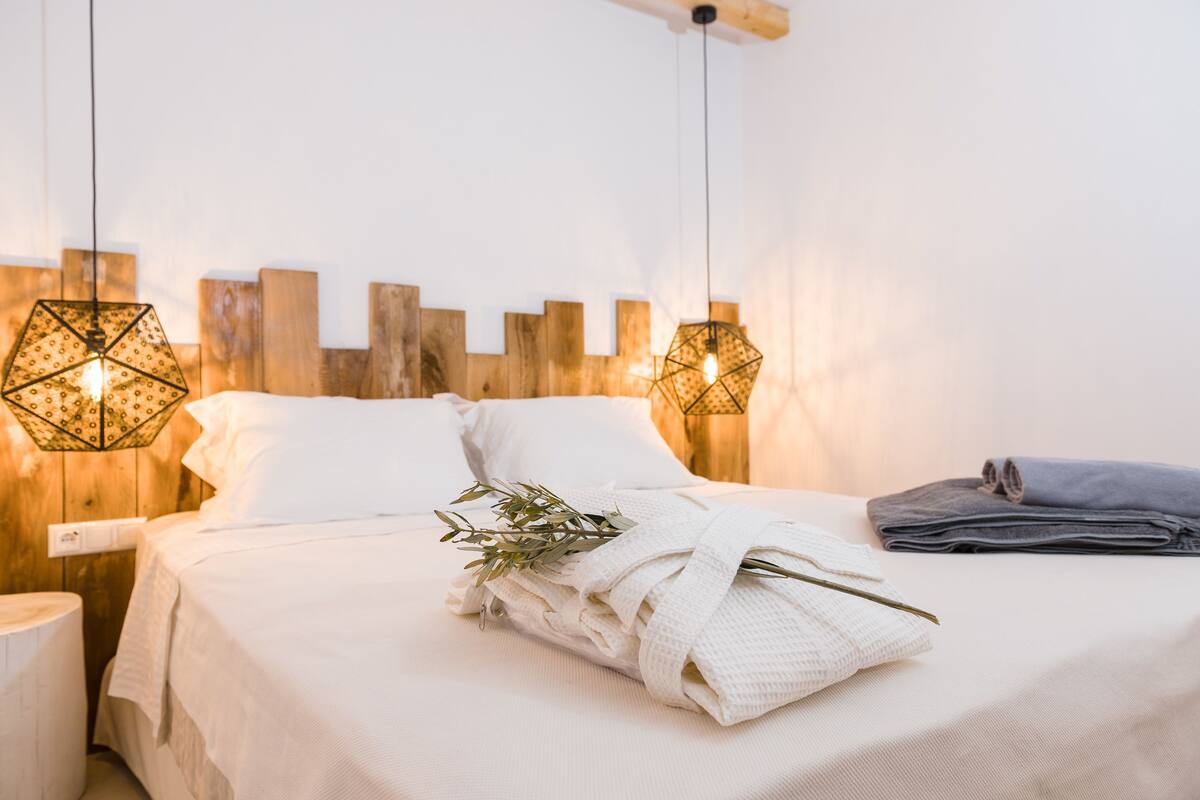 Un lit bien fait, avec du linge de lit blanc, un peignoir plié et une branche de verdure.