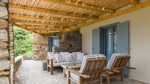 A covered patio with stone flooring, wooden furniture, and a stone fireplace.