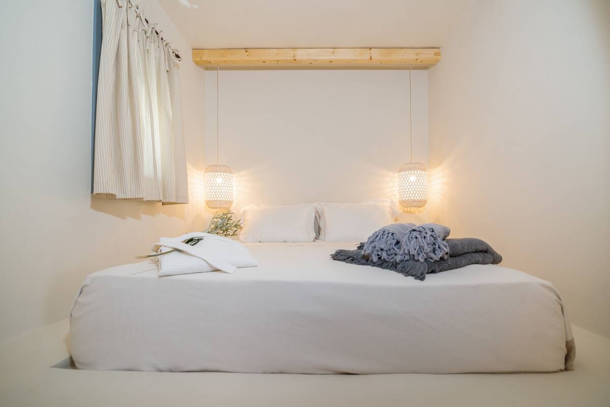 Une chambre à coucher avec un lit, deux lampes fixées au mur, un rideau et une poutre en bois au-dessus du lit.