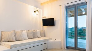 A modern living room with a white sofa, a flat-screen TV mounted on the wall, and a sliding glass door leading to an outdoor area.