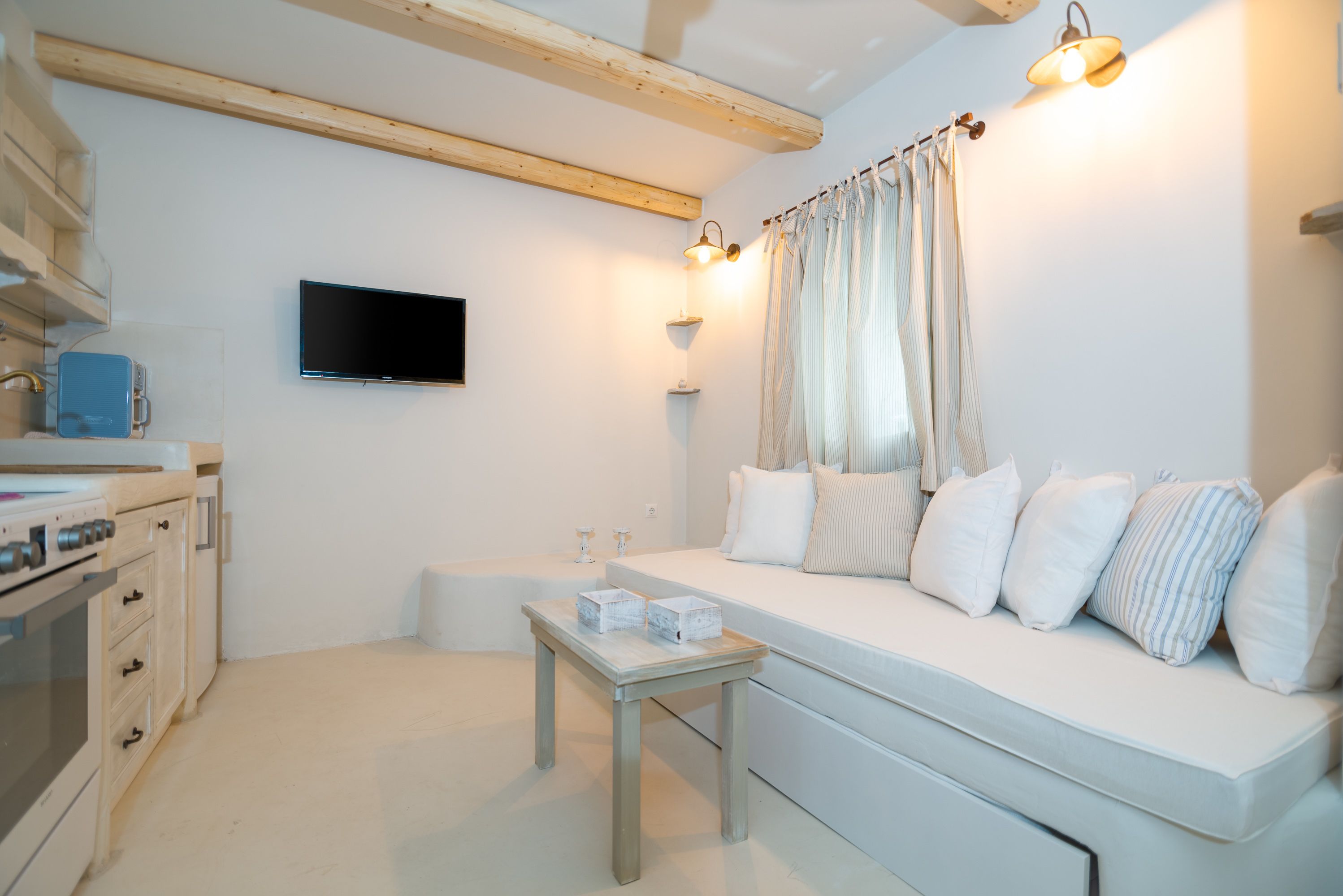 Un salón moderno y minimalista con un sofá blanco, una mesita de madera y un televisor de pantalla plana montado en la pared.
