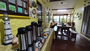 Un comedor con una mesa larga, varias tazas térmicas de acero inoxidable, un pequeño modelo de faro y distintas decoraciones en la pared.