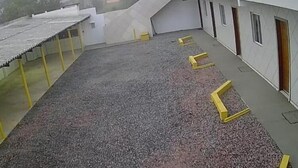 A covered outdoor area with a gravel floor, yellow safety railings, and a building with multiple doors and windows. - Pousadas Mafra (Mafra)