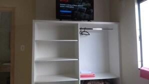 A room with a white shelving unit, a television mounted above it displaying a Netflix logo, and a window on the right side. - Pousadas Mafra (Mafra)