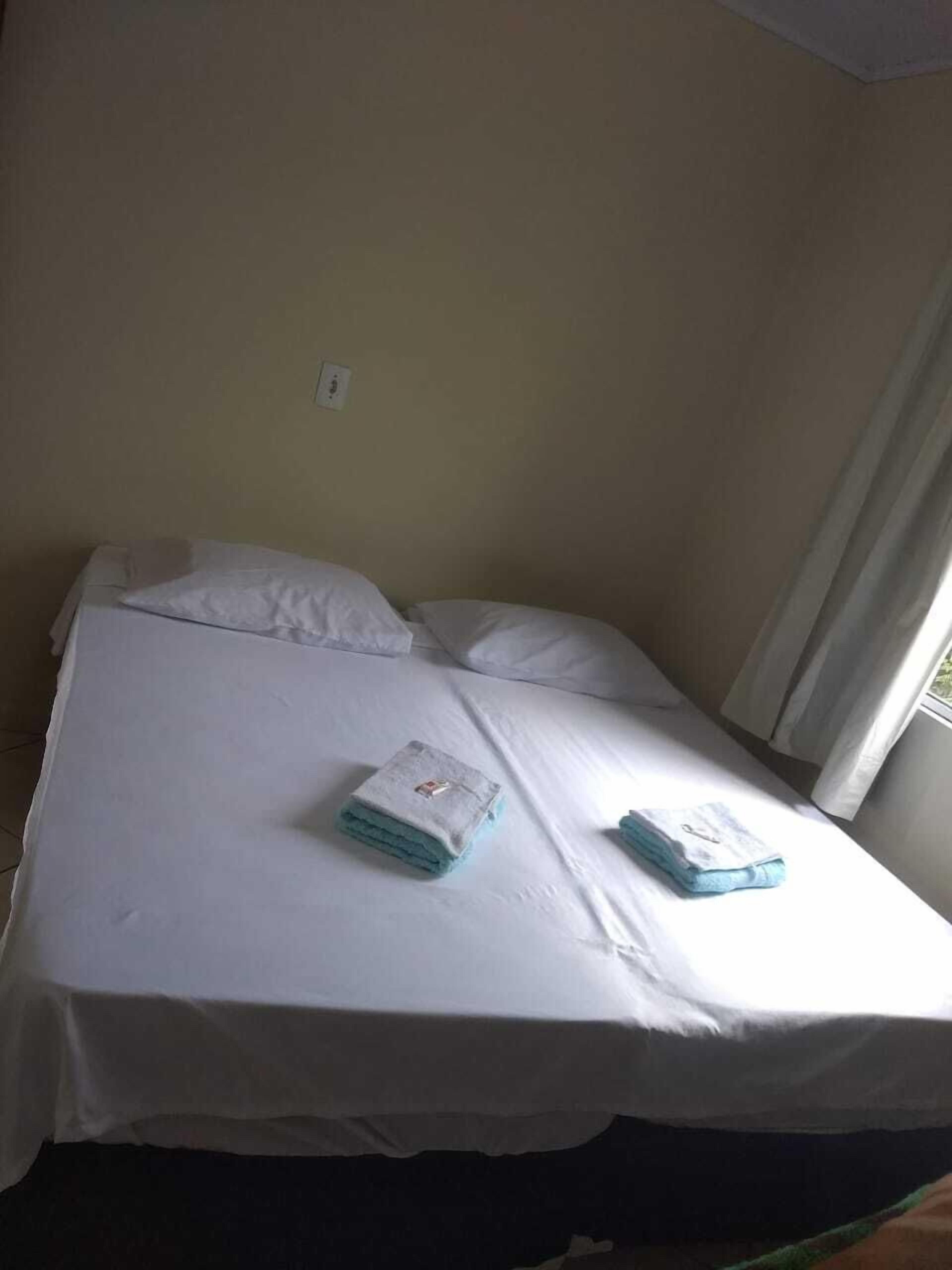 Una cama individual con ropa blanca y dos toallas dobladas.