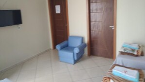 A room with a blue armchair, a bed with a blue and white cover, and a television mounted on the wall. - Pousadas Mafra (Mafra)