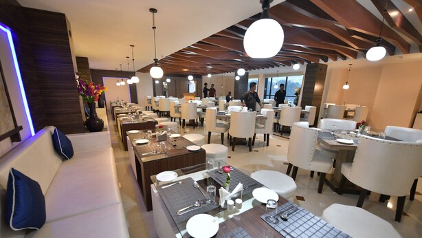 A modern dining area with multiple tables and chairs, a sofa with blue cushions, and a vase with flowers. - Hotel  Himalaya (Sidli)