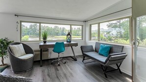 Une véranda aménagée avec un bureau, deux chaises, un canapé et une plante en pot.