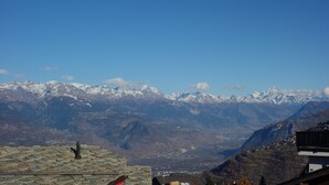 A mountain view with snow-capped peaks, a stone roof, and a small building in the foreground.