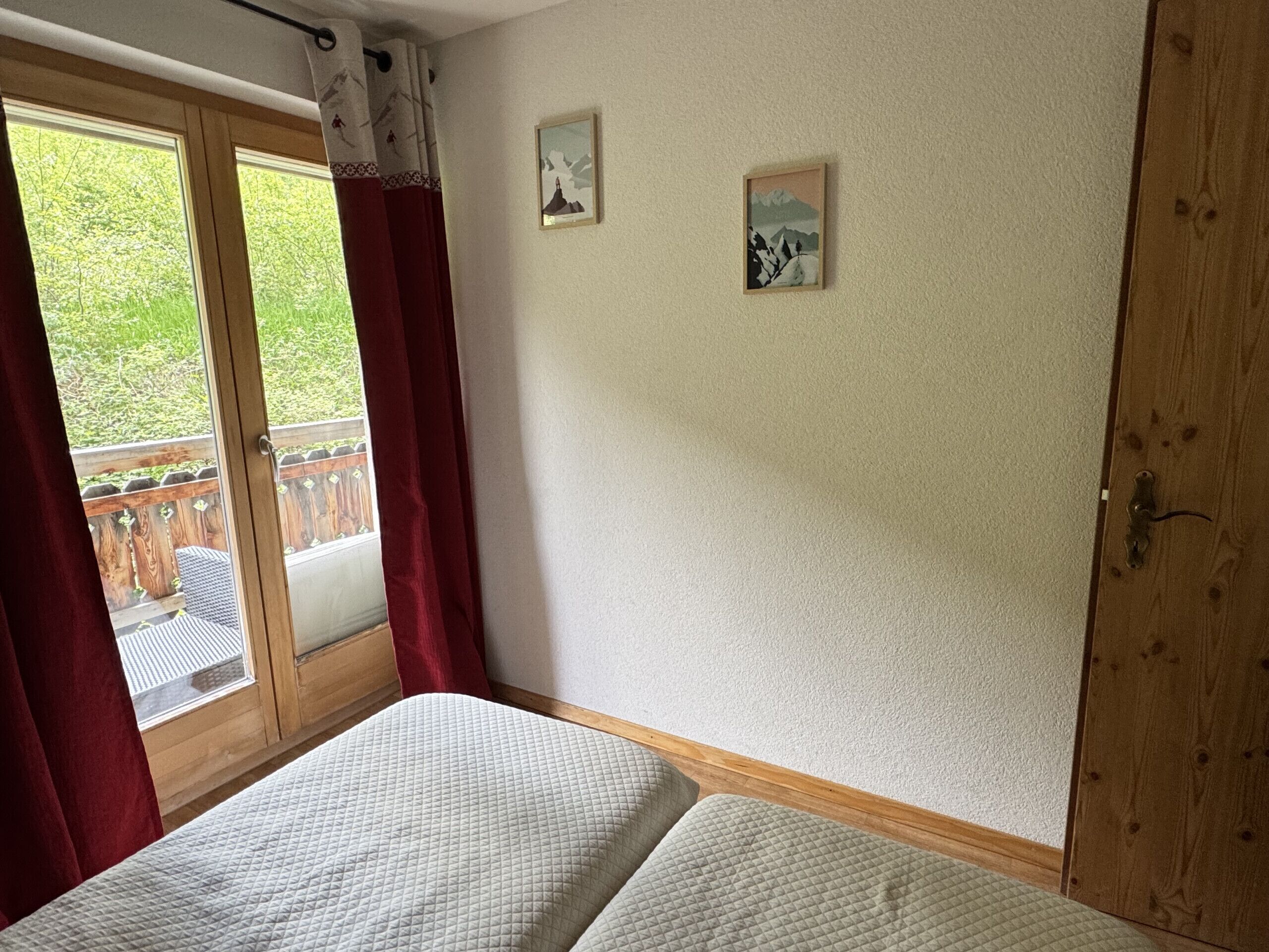 Un dormitorio con cama, una puerta de madera y vistas a un balcón con cortinas rojas.