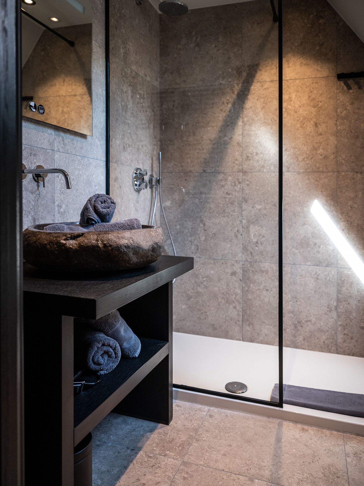 A modern bathroom with a stone sink, a mirror, and a glass shower enclosure.