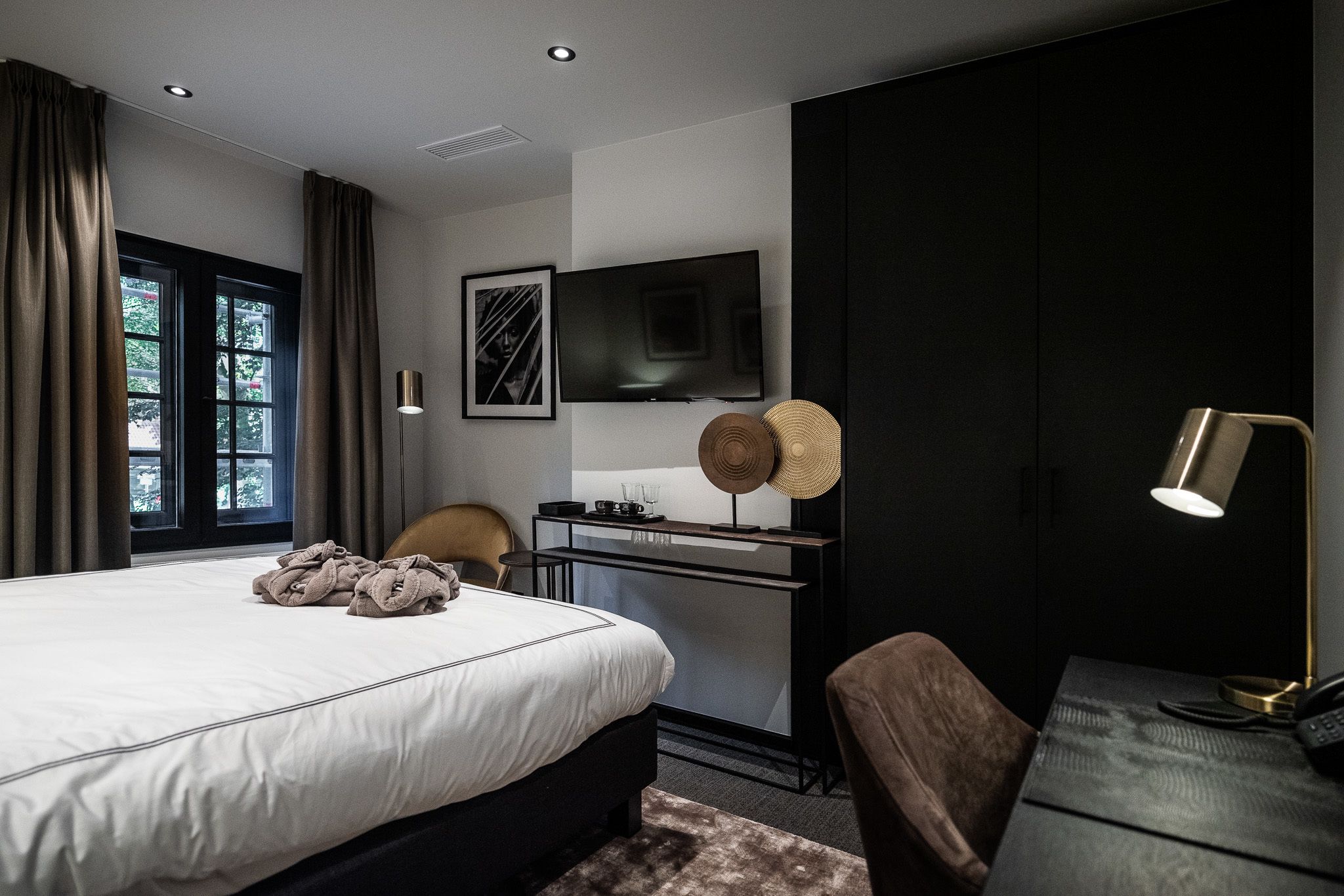 A modern hotel room with a large bed, a desk with a flat-screen TV, a chair, and a lamp.