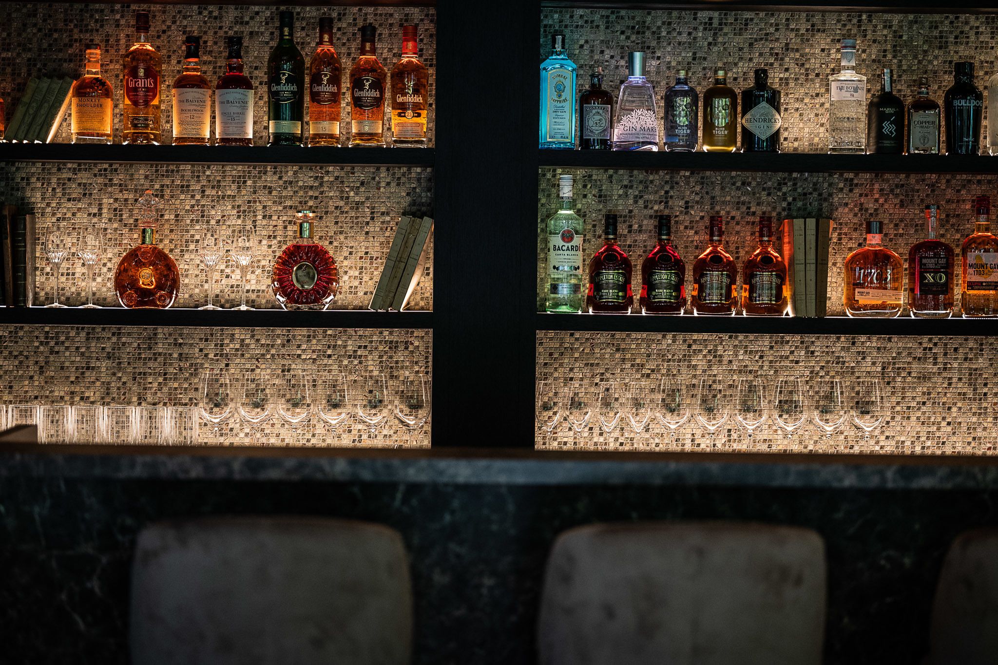 Un bar avec des étagères remplies de bouteilles de différentes sortes d’alcool et de verres.