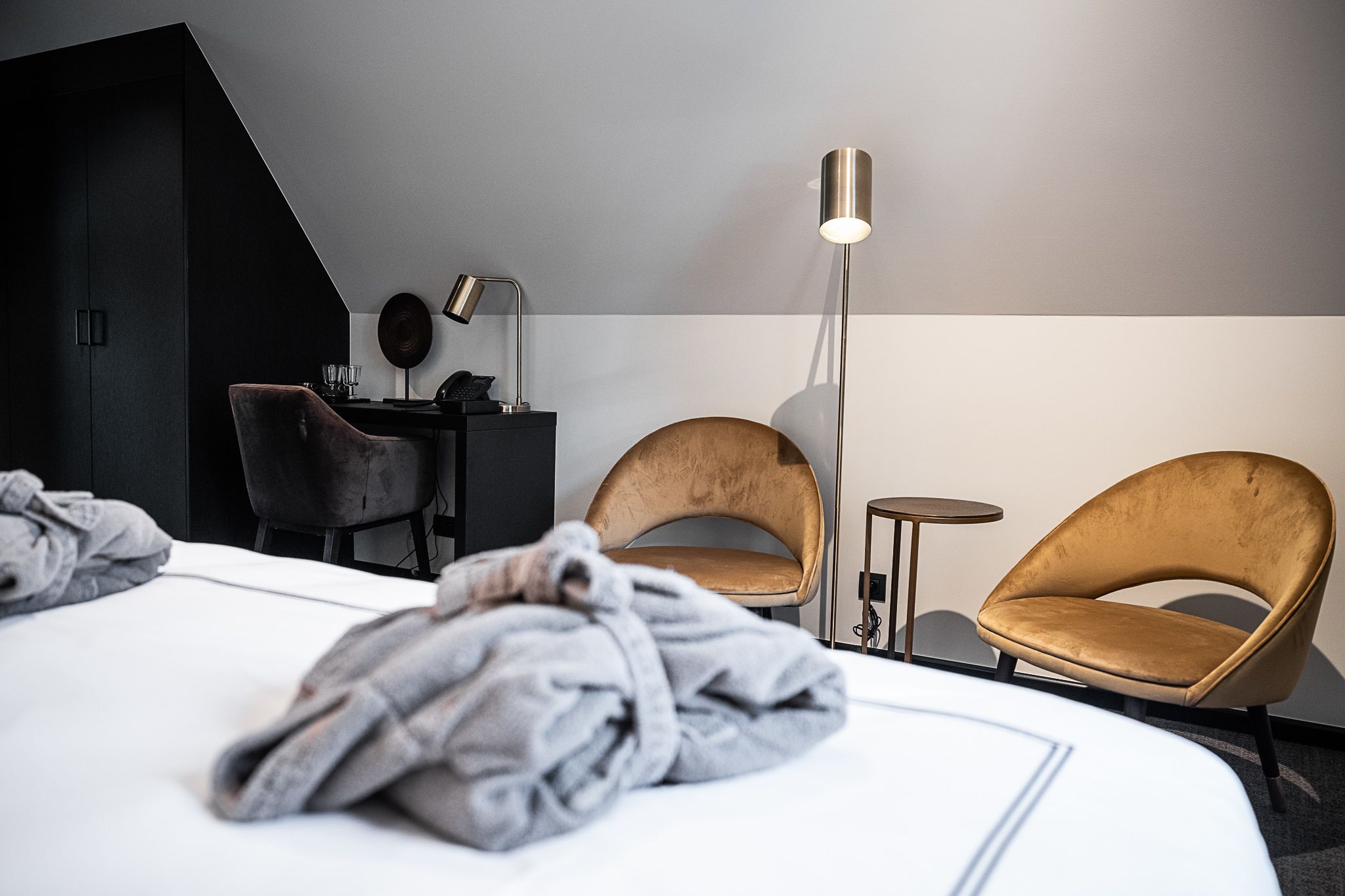 Habitación de hotel moderna con cama, dos sillones, escritorio con lámpara y una mesita.