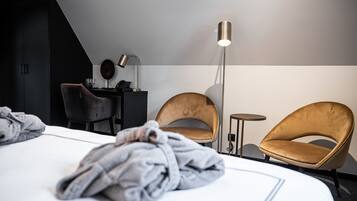 Habitación de hotel moderna con cama, dos sillones, escritorio con lámpara y una mesita.