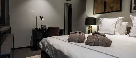A hotel room with a large bed, a desk with a lamp, a chair, and a painting on the wall.