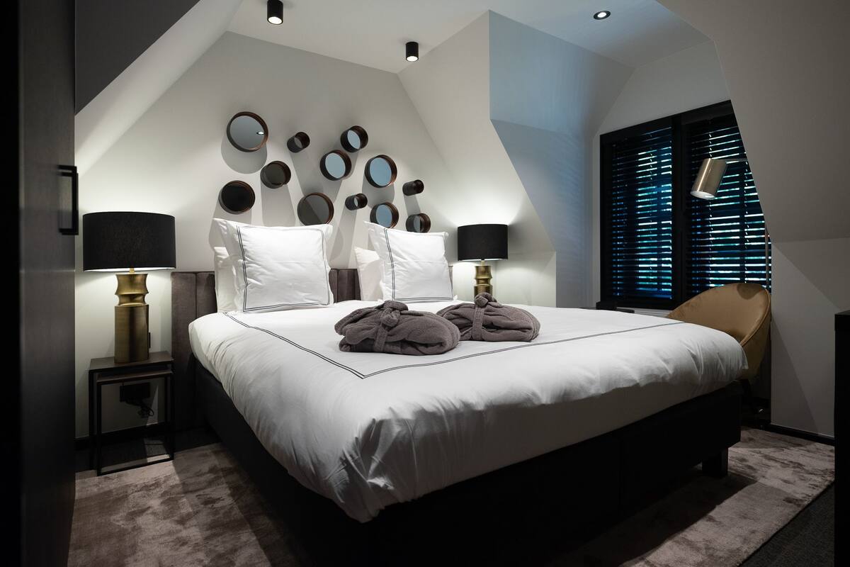 A modern bedroom with a large bed, multiple wall-mounted mirrors, and two bedside lamps.