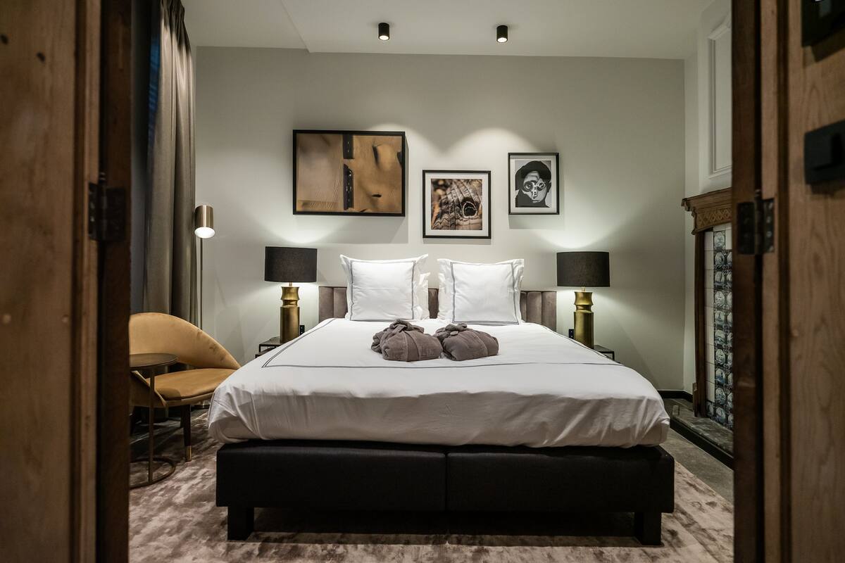 A neatly arranged bedroom with a large bed, bedside lamps, a chair, and artwork on the walls.