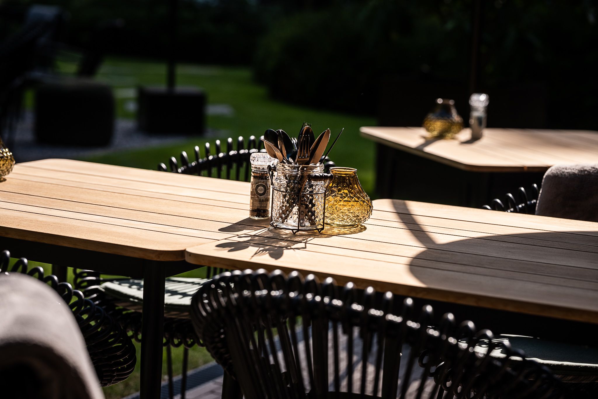 Outdoor dining tables with metal chairs and glass containers with utensils.