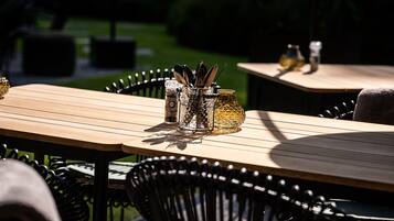 Outdoor dining tables with metal chairs and glass containers with utensils.