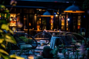 An outdoor seating area with wicker chairs and tables, illuminated by hanging lamps. - Boutique Hotel 't Fraeyhuis (Bruges)
