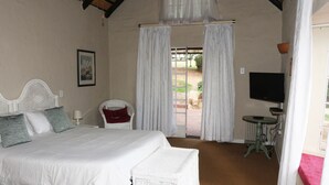 A bedroom with a bed, a television, a small table, and a chair. - Sterkfontein Heritage Lodge (Krugersdorp)
