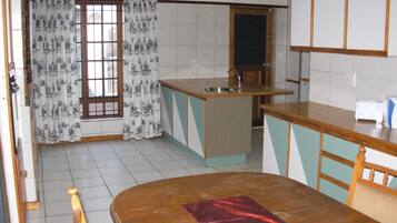 A kitchen with a wooden dining table, a small island with a sink, and a window with patterned curtains.