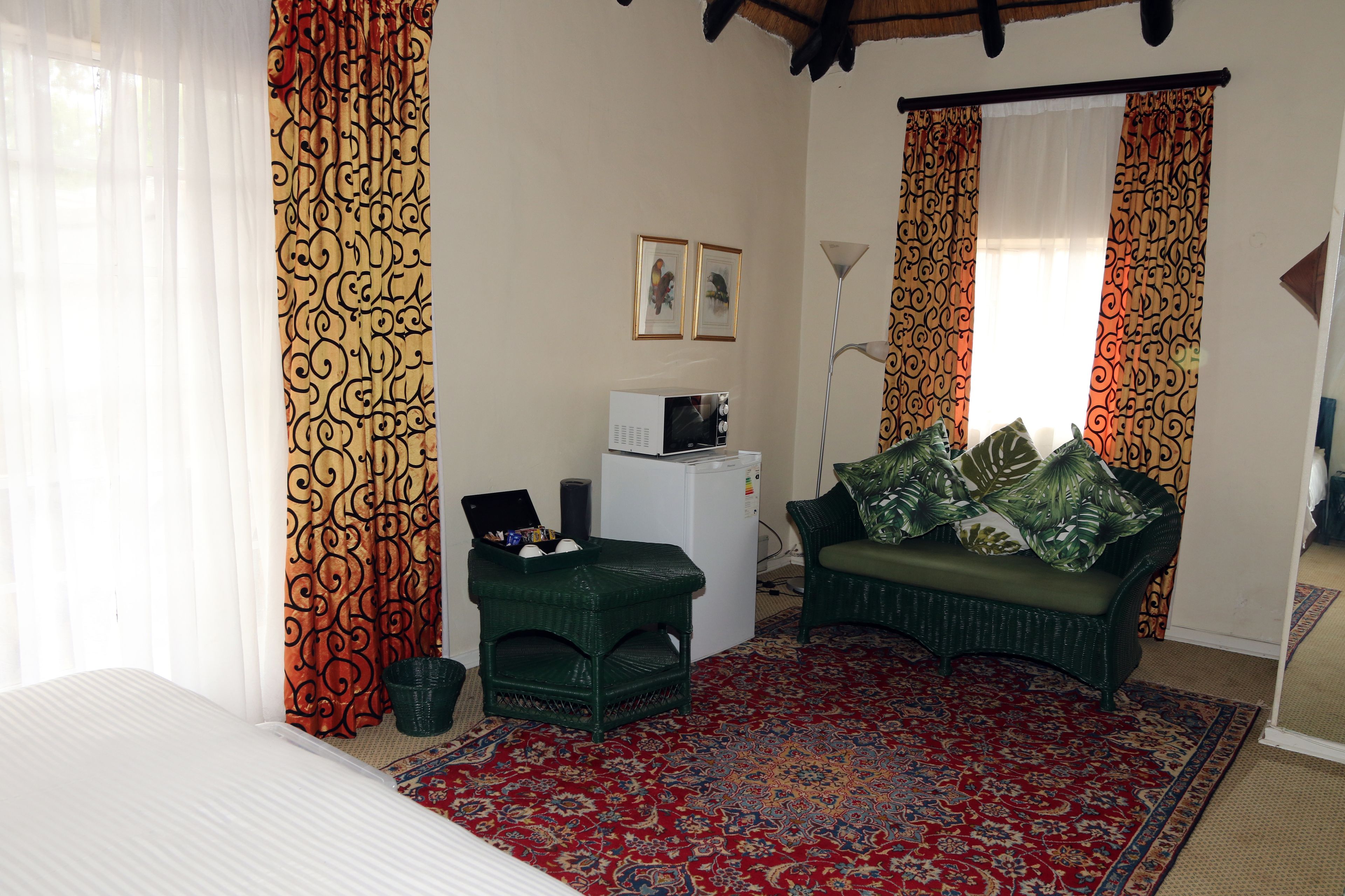Quarto com uma cama, um pequeno frigorífico branco, um sofá verde com almofadas, um tapete estampado e cortinas com padrão espiralado.
