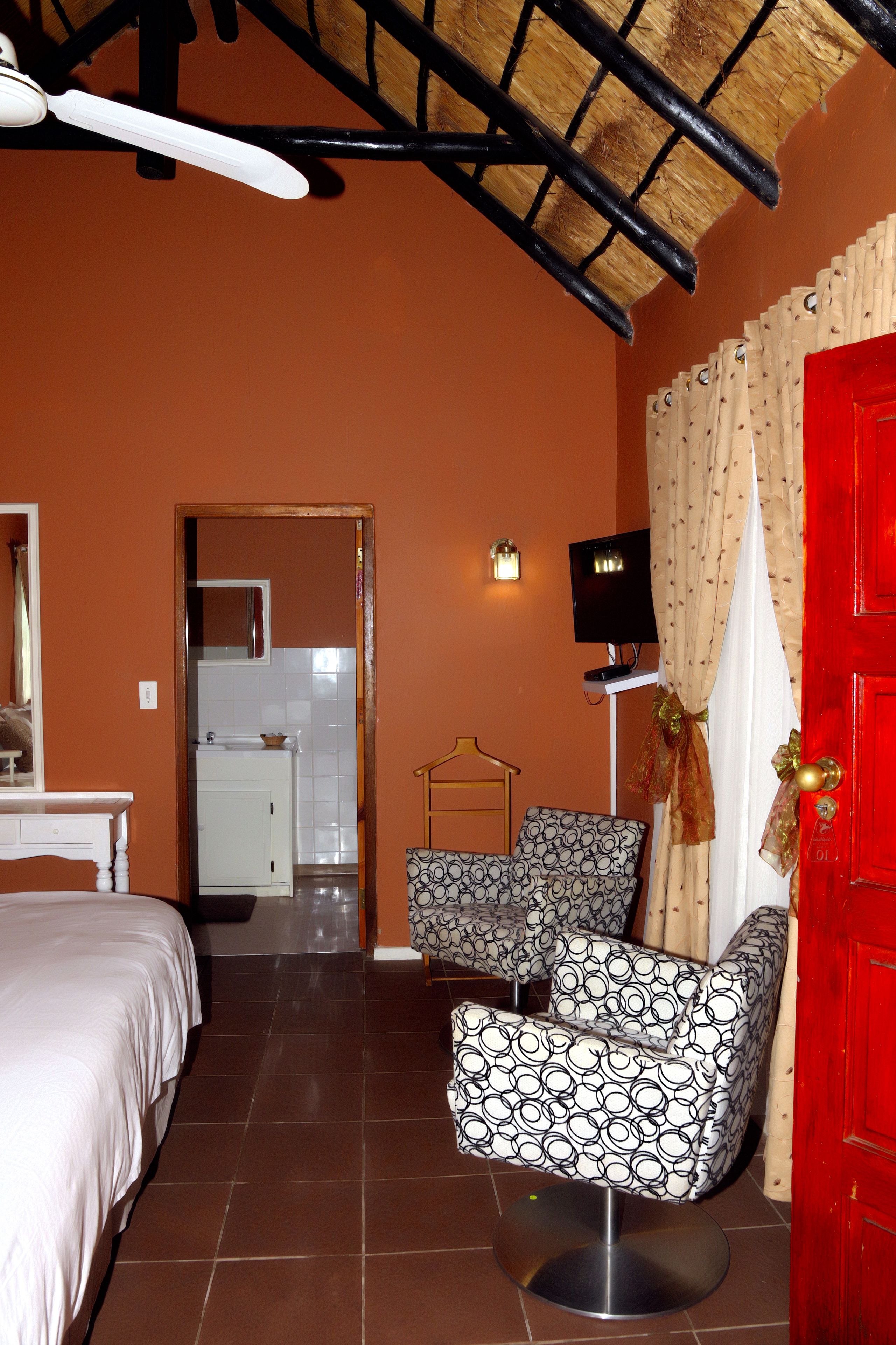 Une chambre d’hôtel avec un lit, deux fauteuils à motifs, une porte rouge et un téléviseur.