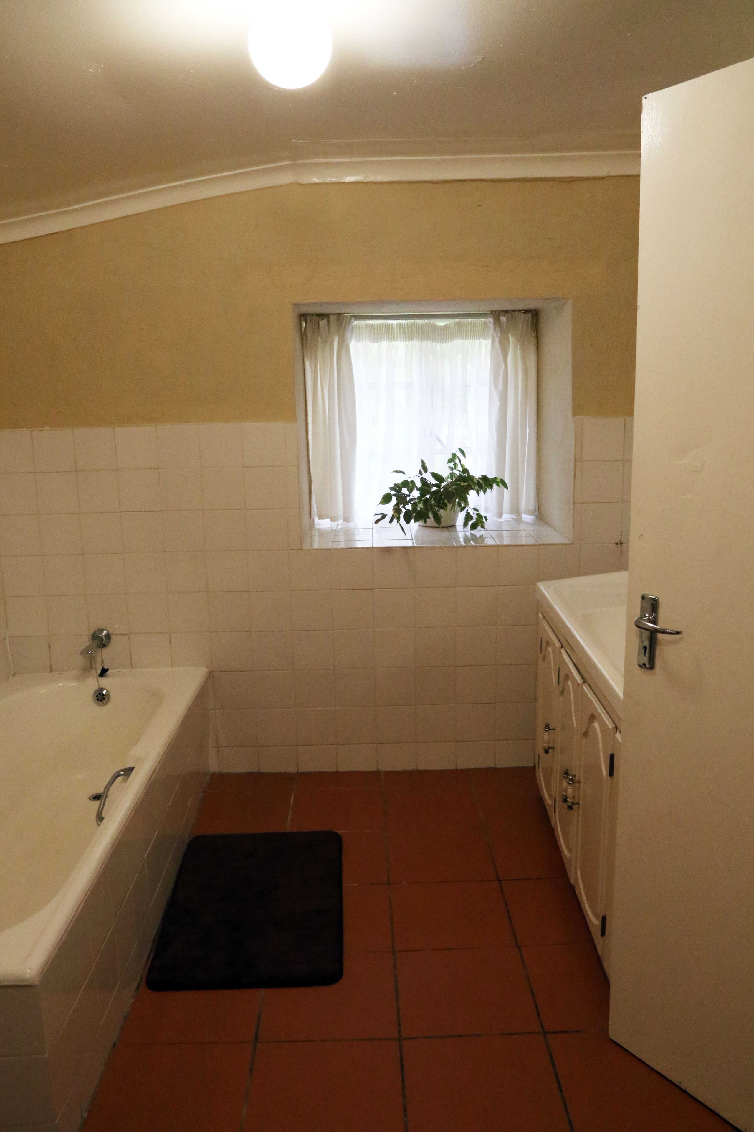 Un baño con bañera, ventana con cortinas, planta en maceta y una puerta.