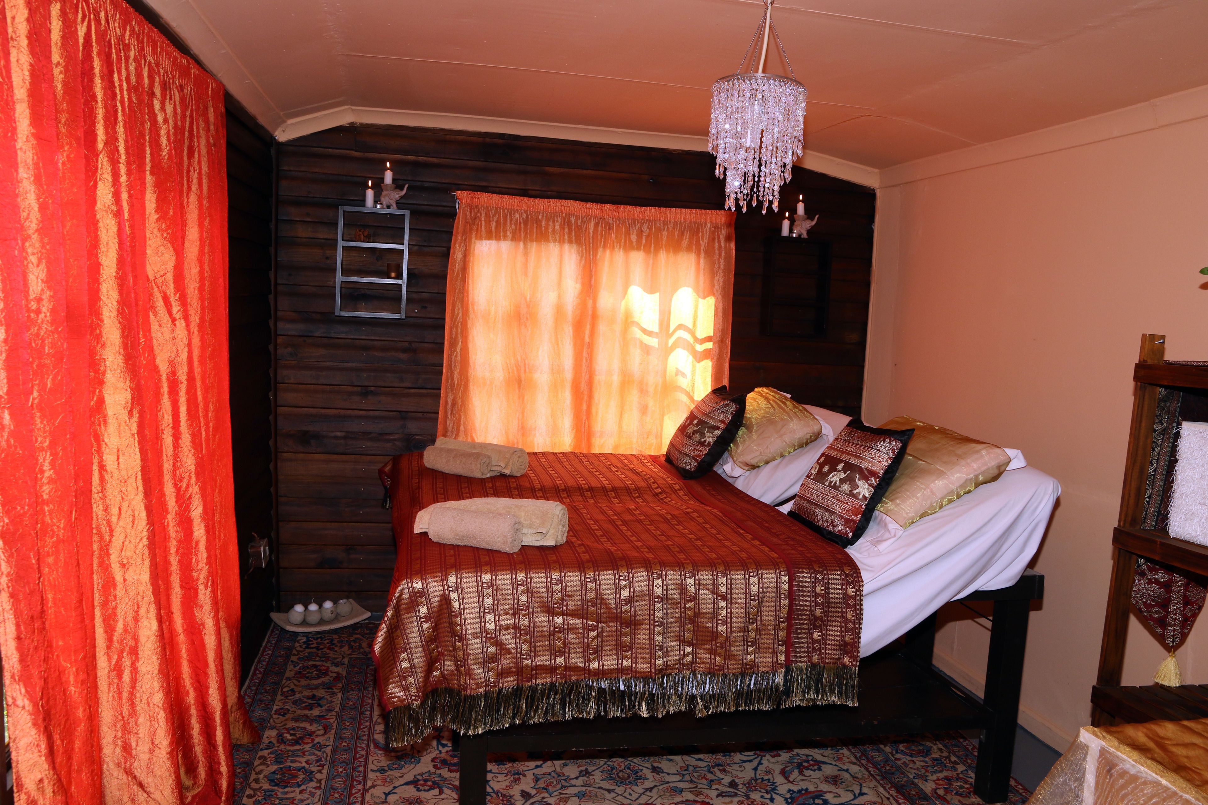 A bedroom with a wooden headboard, a bed with patterned bedding, a chandelier, and a red curtain.