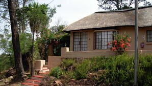 A house with a thatched roof, a stone staircase leading to the entrance, and a well-maintained garden with various plants and flowers. - Sterkfontein Heritage Lodge (Krugersdorp)