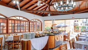 A restaurant with wooden tables and chairs, a buffet counter, and large windows with arched tops. - Elite Hotel (Florianópolis)