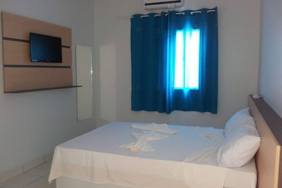 Una habitación de hotel con una cama, un televisor montado y una ventana con cortinas azules.