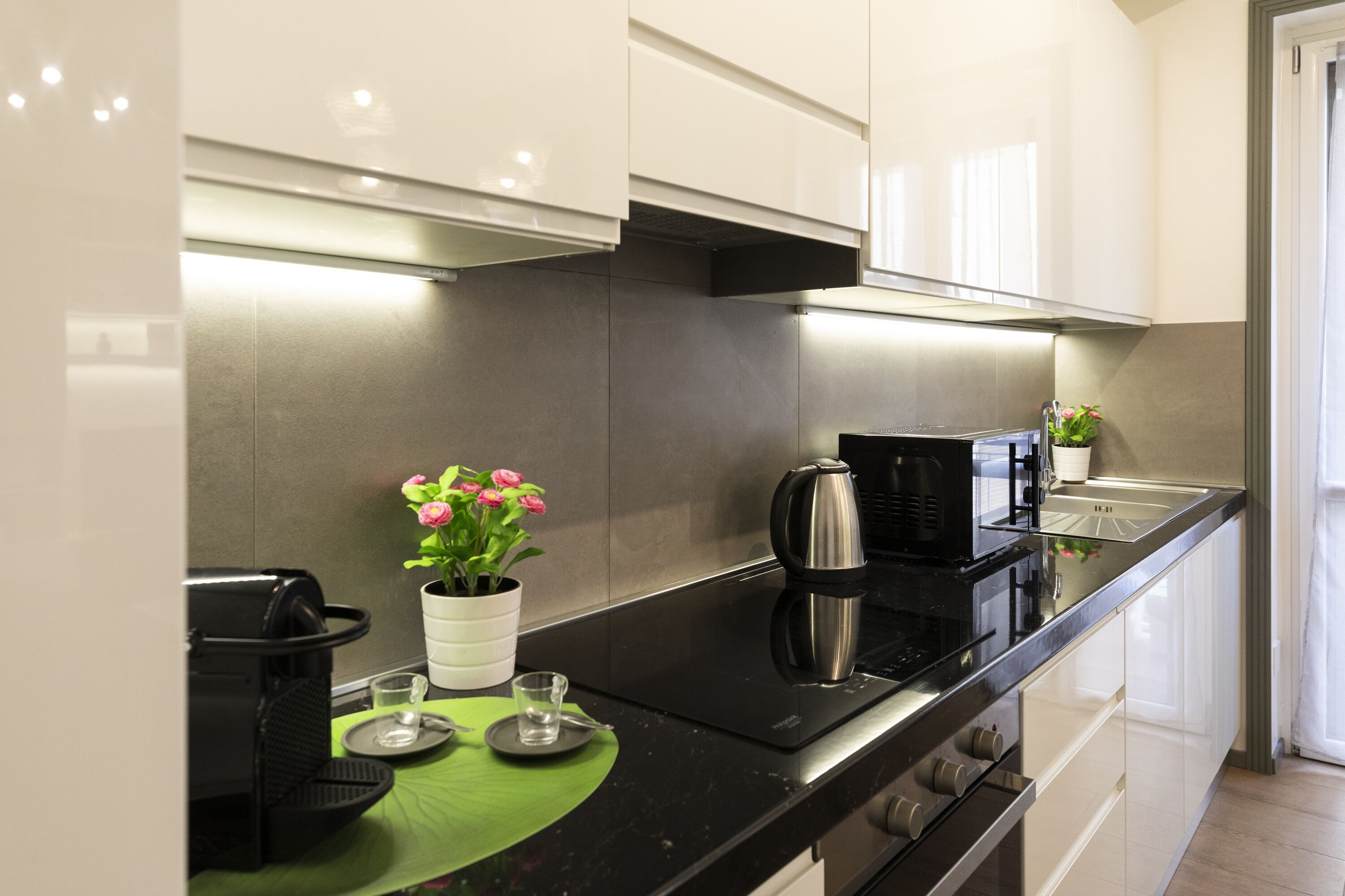 Una cocina moderna con electrodomésticos de acero inoxidable, encimera negra y armarios blancos.